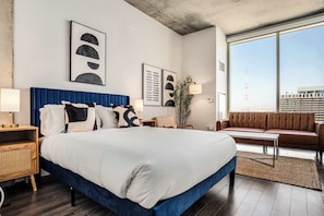 A modern hotel room with a large bed, a sofa, a desk, and a large window offering a city view. - Boulevard Stays Highrise STU Sky Pool, Parking, Gym 43 (Phoenix)