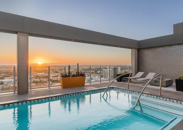 A rooftop pool with a city view at sunset, lounge chairs, and a planter with plants. - Boulevard Stays Highrise STU Sky Pool, Parking, Gym 43 (Phoenix)