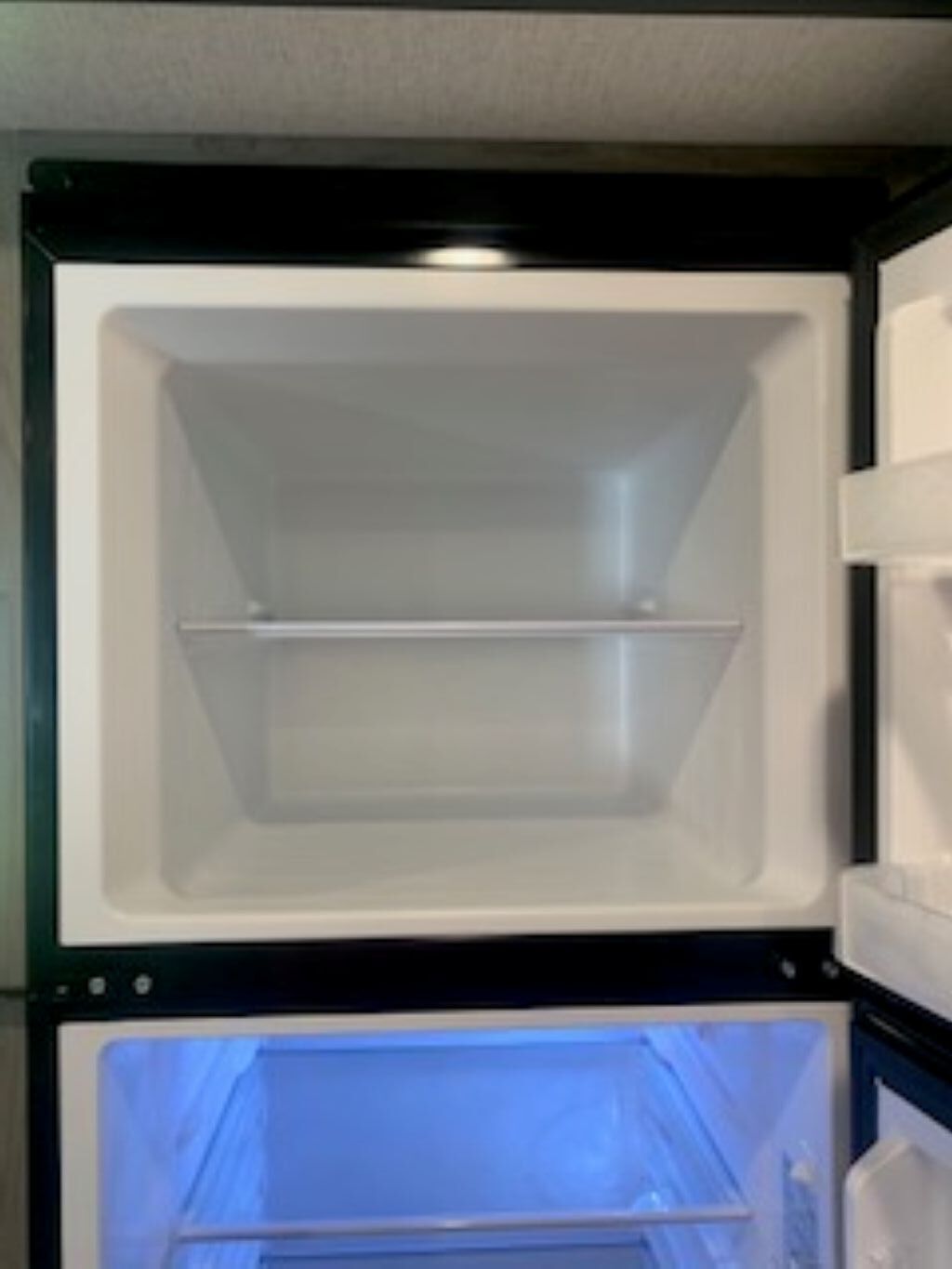 Ein offener Kühlschrank mit zwei Ablagen und einem Gefrierfach.