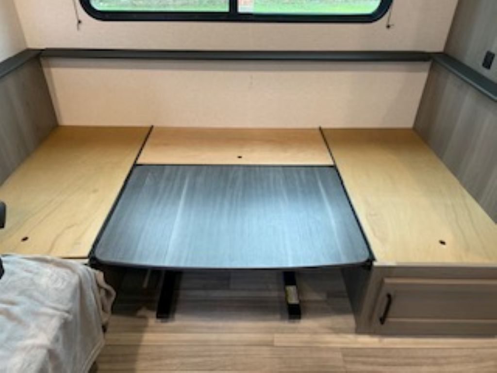 Un intérieur de camping-car compact comprenant un cadre de lit en métal, une petite table en bois et une fenêtre.