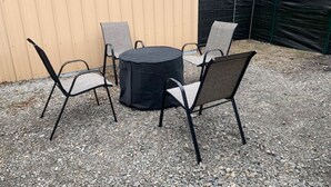 En terrasse med et rundt bord og fire stole, en sort parasol og et træhegn i baggrunden.