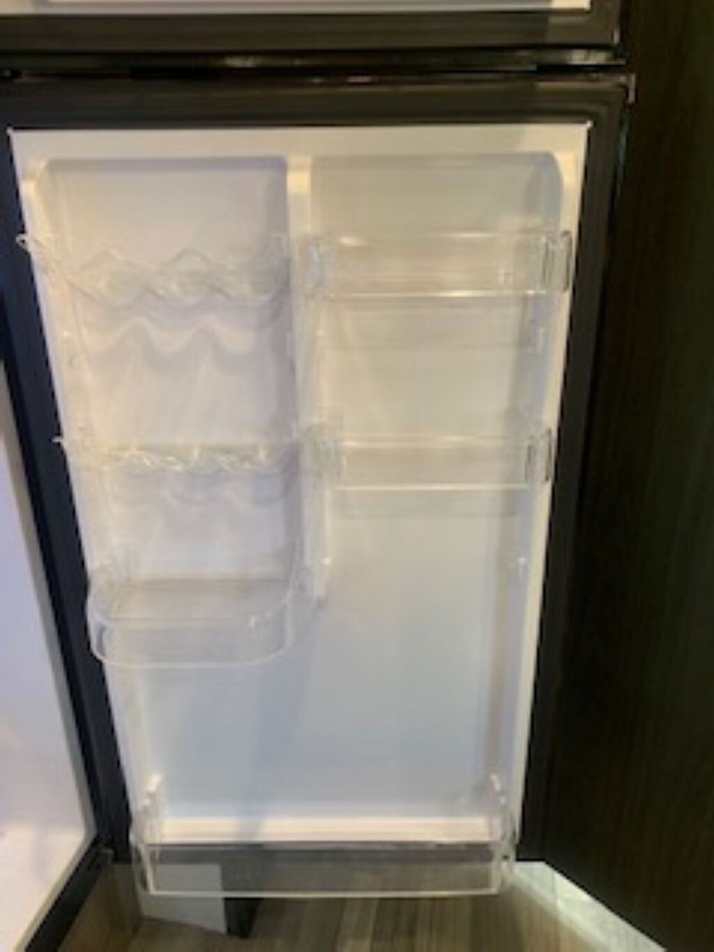 An open refrigerator with clear plastic shelves and a freezer compartment.