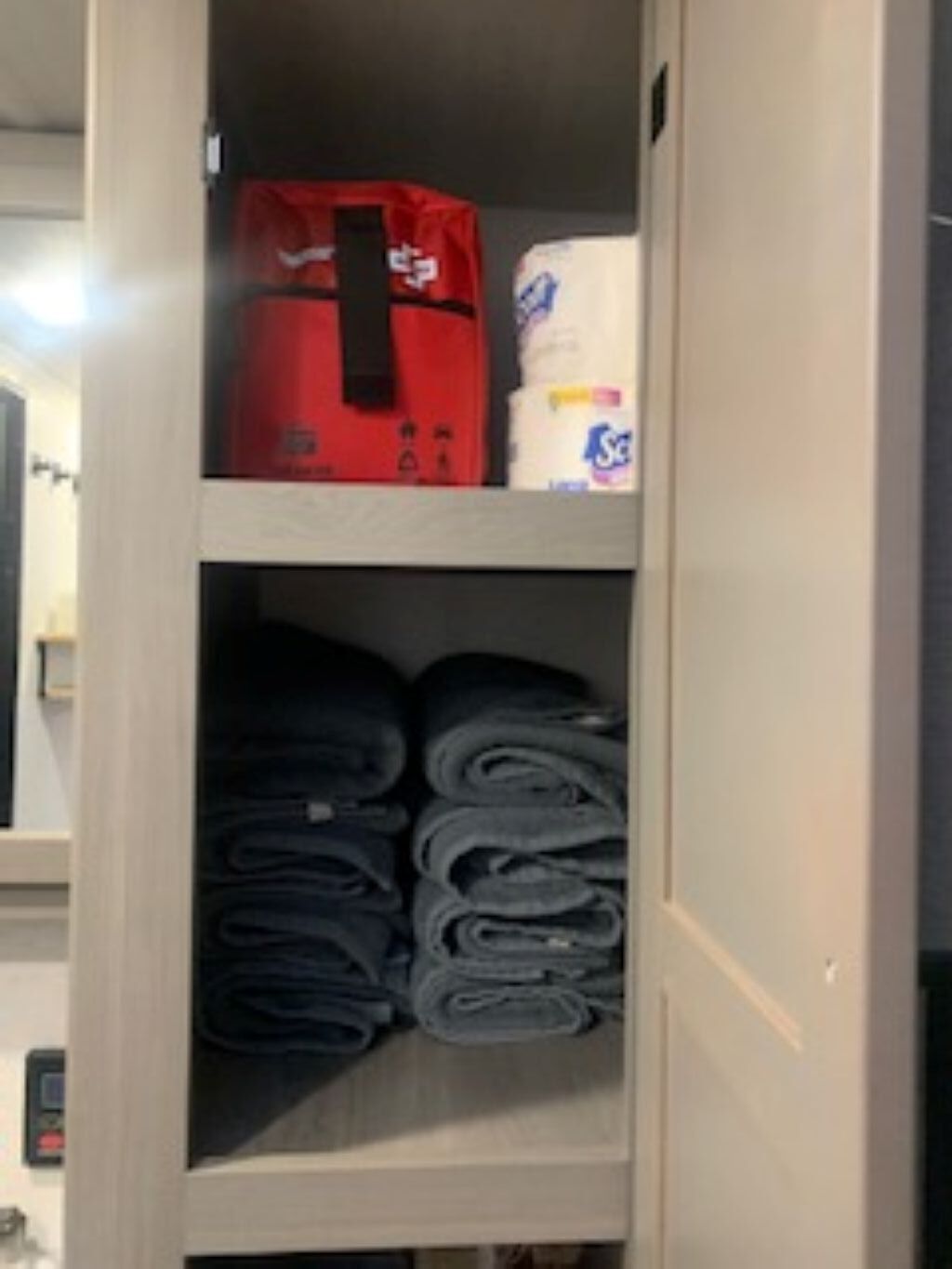 A storage compartment with folded towels and a red bag.