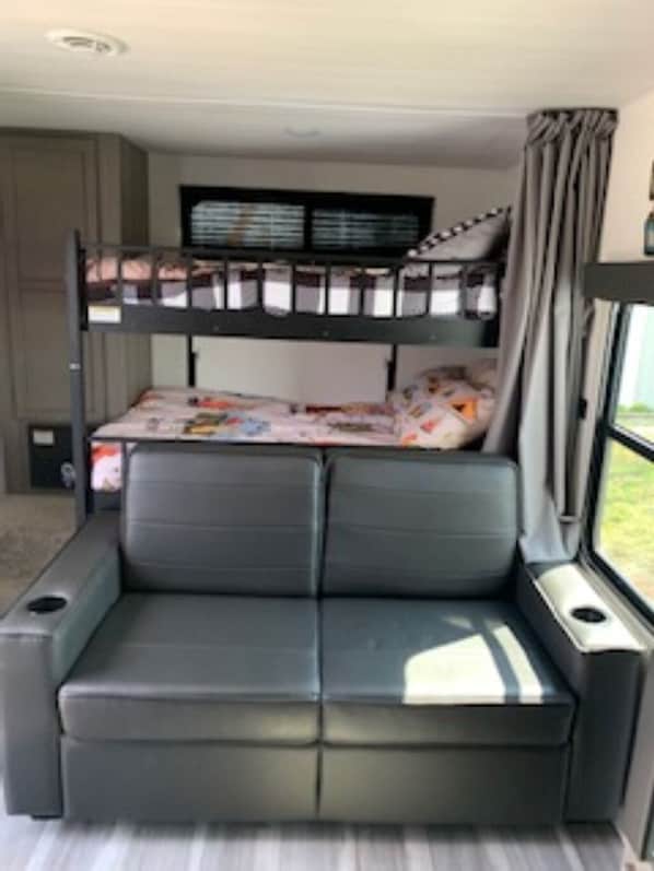 Un lit superposĂ© avec un lit en bas, un canapĂ©, une fenĂȘtre avec des rideaux et une petite table.