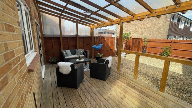 A covered patio with wooden flooring, a seating area with black furniture, and a hanging blue dolphin decoration. - Tranquil Home Retreat (Berinsfield)