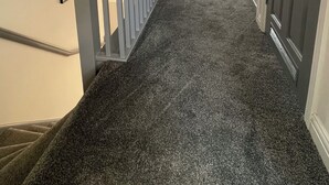 A hallway with a carpeted floor, a staircase with a railing, and a door leading to a bathroom. - Tranquil Home Retreat (Berinsfield)