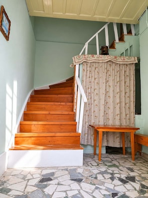 A wooden staircase with a white railing, a floral curtain, a small wooden table, and a tiled floor. - Cozy Stay in Chios Near the Beach Private Balcony (Chios)