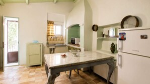 Uma cozinha com mesa, geladeira, pia e janela com cortinas.