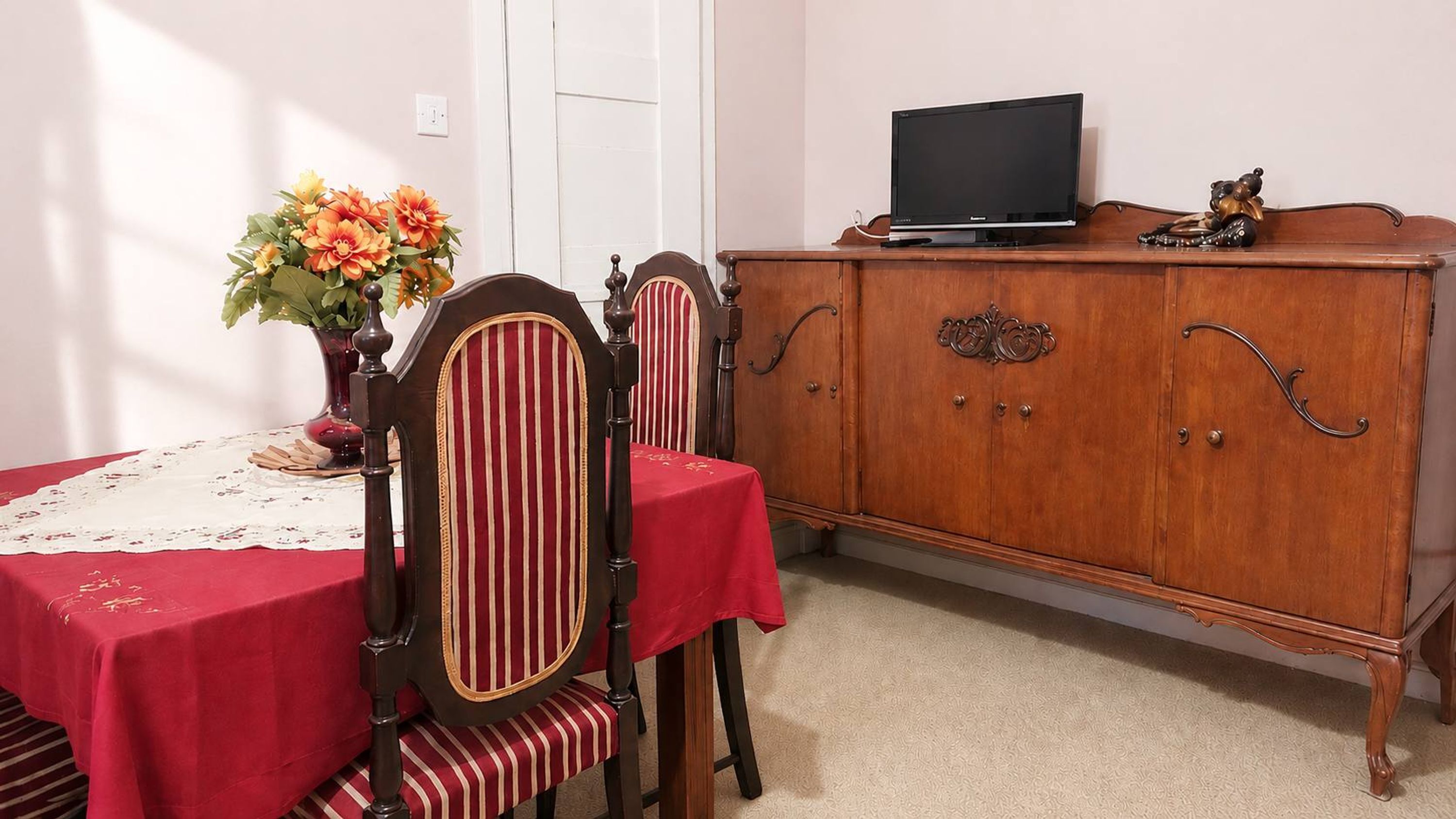 Een eetruimte met een tafel voor twee personen, een houten kast en een televisie erboven.