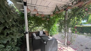 Um pátio externo com mobiliário de vime, uma pérgula e vegetação exuberante.