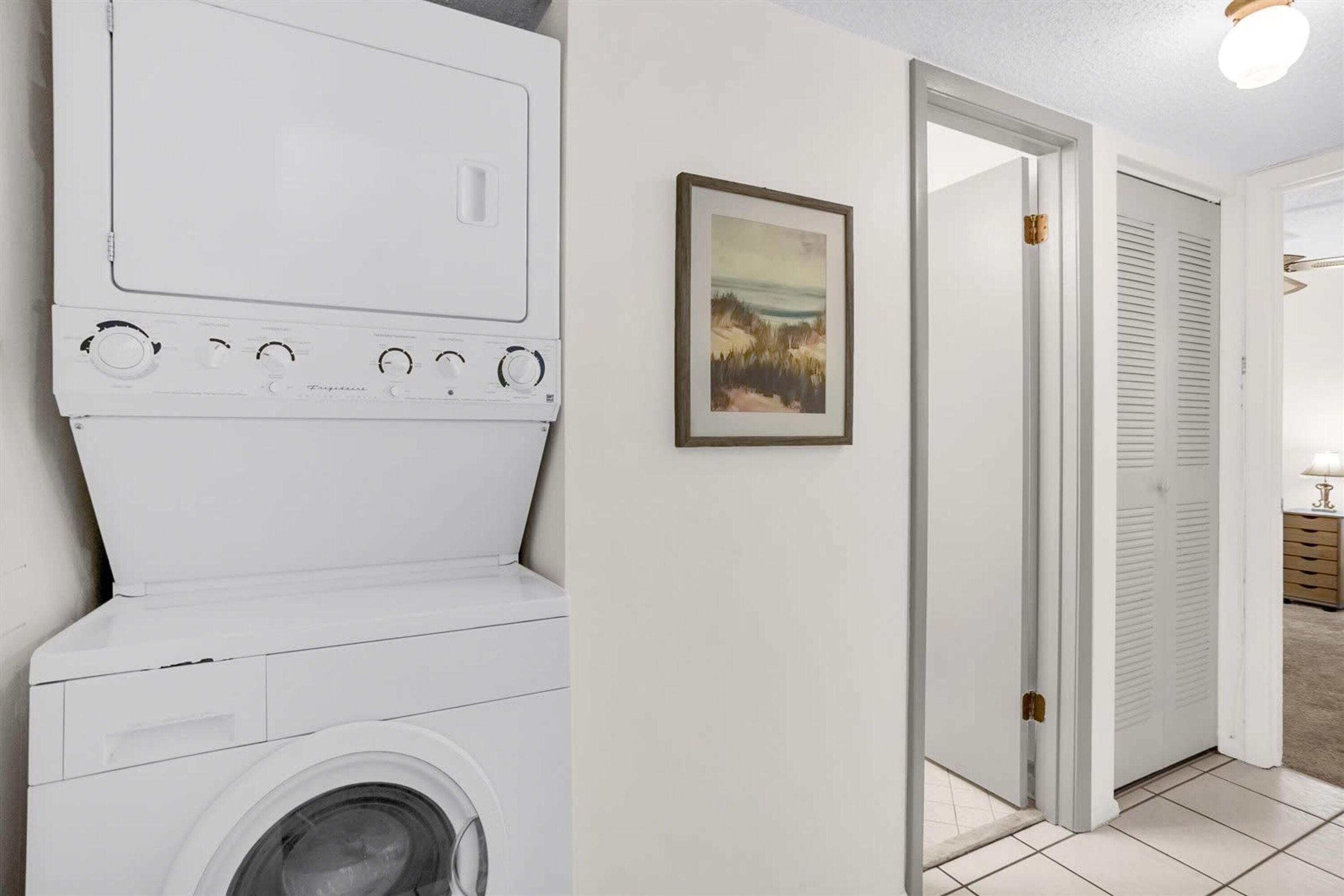 Een wasruimte met een wasmachine en droger, een inlijsting foto aan de muur, en een deur die naar een andere ruimte leidt.