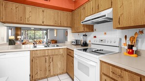 Een keuken met houten kastjes, een witte kookplaat en een groot raam.