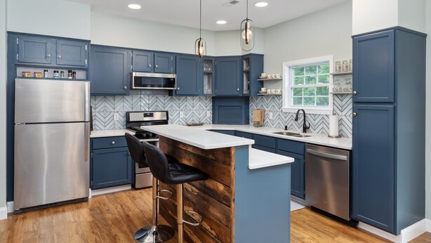 A modern kitchen with dark blue cabinets, stainless steel appliances, a wooden island with a bar stool, and pendant lighting. - Dog Friendly, Beautiful Views, Hot tub! (Rileyville)