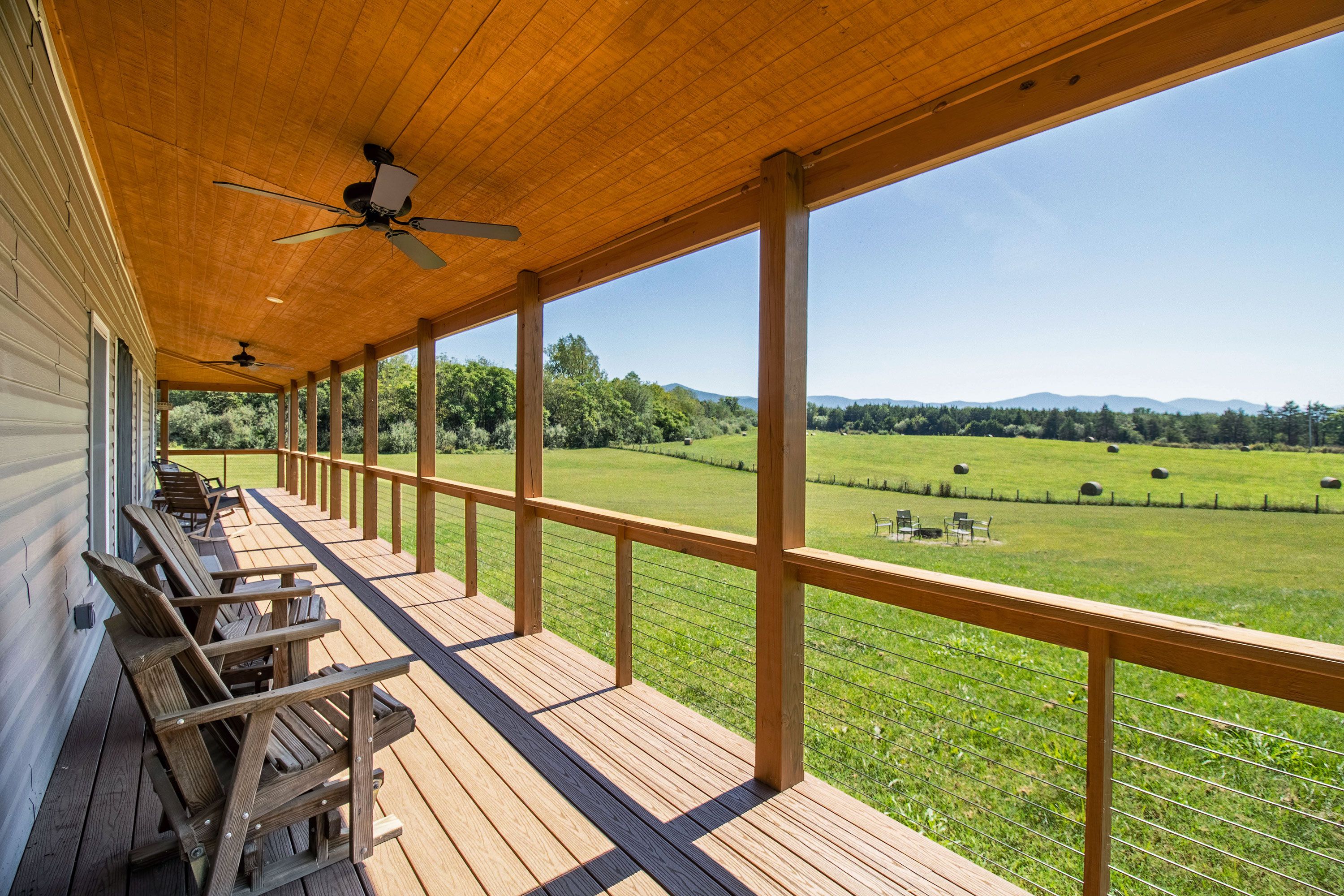 A covered deck with wooden railings and chairs, overlooking a green field.
