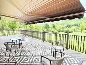 Um deck coberto ao ar livre com tapete estampado, cadeiras de vime e vista para uma paisagem verde.