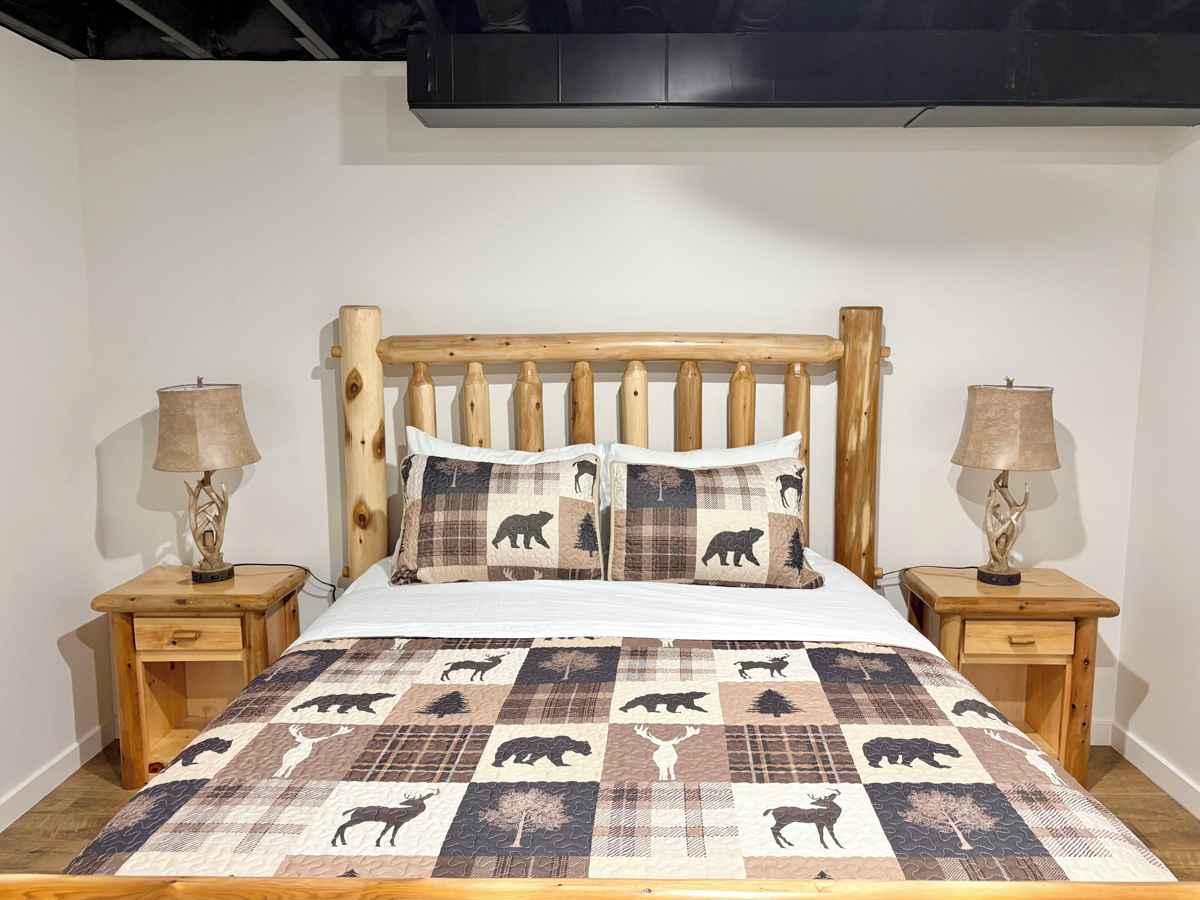 Een bed met een houten hoofdbord, twee nachtkastjes met lampen, en een sprei met dierenprint.