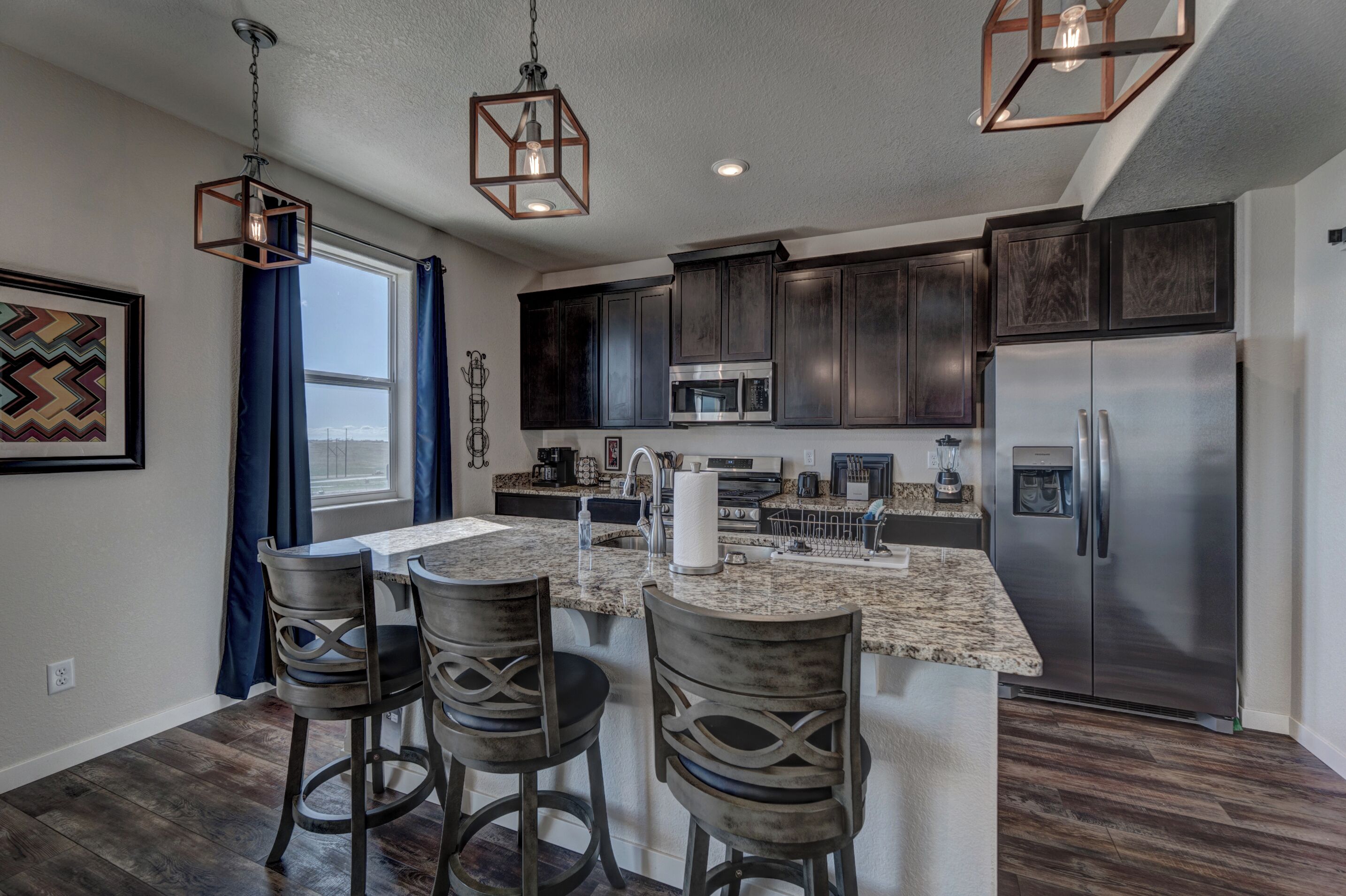 A modern kitchen with dark cabinets, stainless steel appliances, and a central island with bar stools.