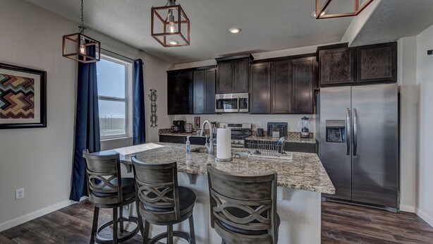 A modern kitchen with dark cabinets, stainless steel appliances, and a central island with bar stools. - Executive Stay for Work & Family (Rapid City)