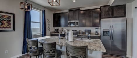 A modern kitchen with dark cabinets, stainless steel appliances, and a central island with bar stools.