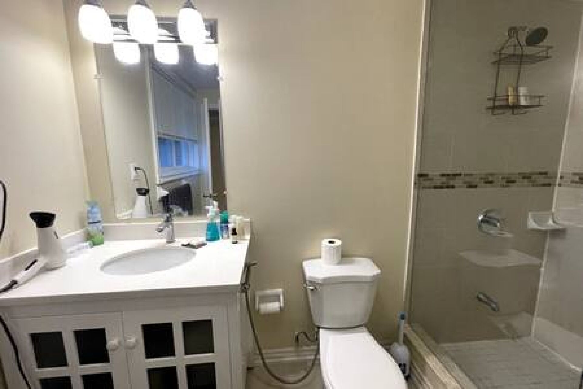Een badkamer met een wit wastafelmeubel, spiegel en toilet. Er is een douchecabine met een glazen deur.