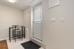 A hallway with a white door, a small table with chairs, and a black rug.