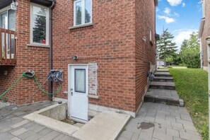 A brick house with a white door, a small front yard, and a paved driveway. - Walk-out Studio Basement Apartment (Mississauga)