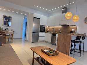 Eine moderne Küche mit weißen Schränken, einem Edelstahl-Kühlschrank, einer Holzinsel mit Barhocker und Pendelleuchten.