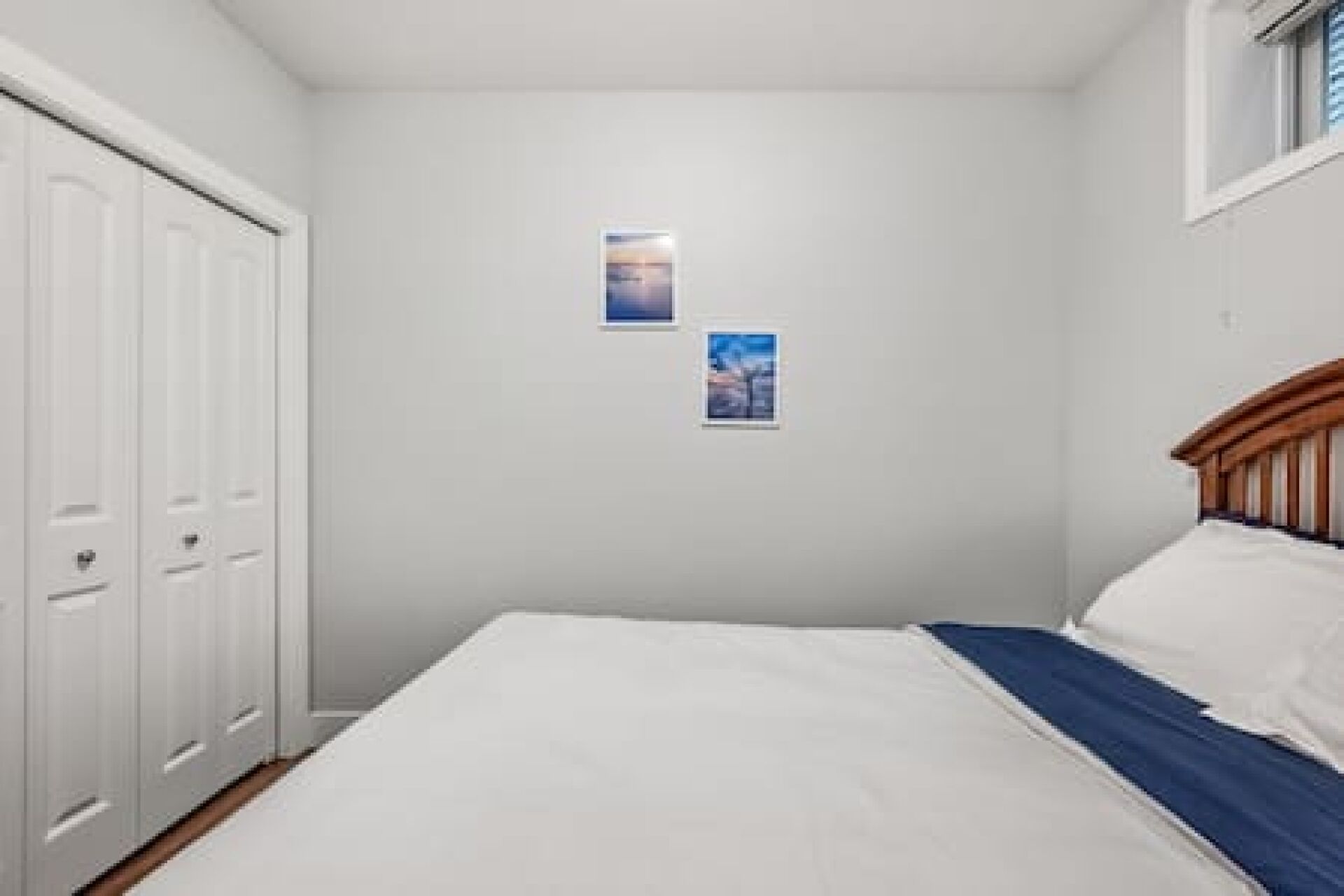 A bedroom with a bed, a wardrobe, and two framed pictures on the wall.