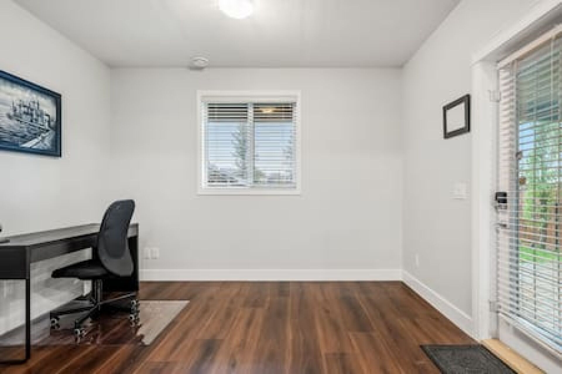 Una habitación con escritorio, silla, ventana y puerta con panel de vidrio.