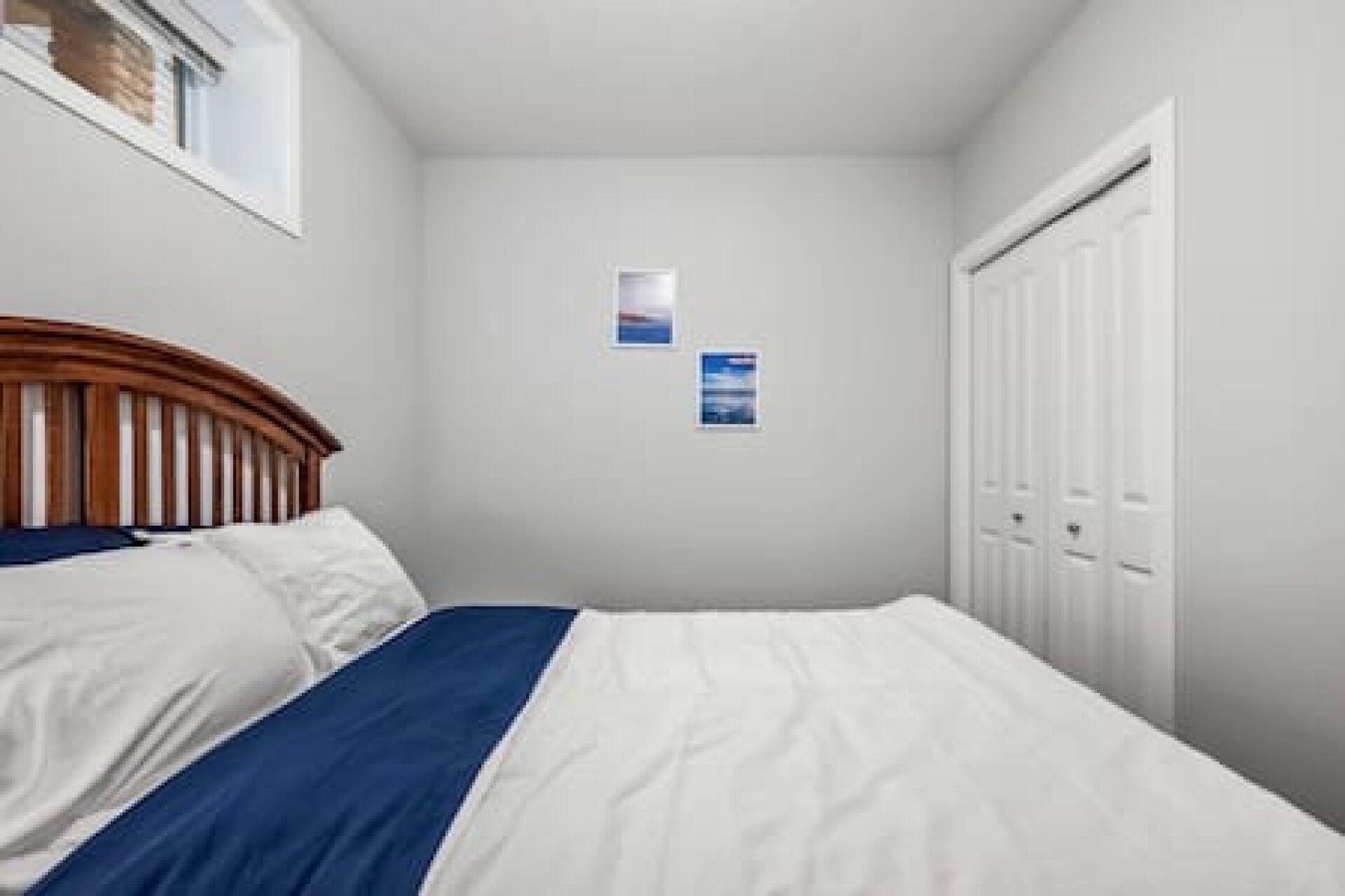 A bedroom with a bed, a window, a door, and two wall-mounted pictures.