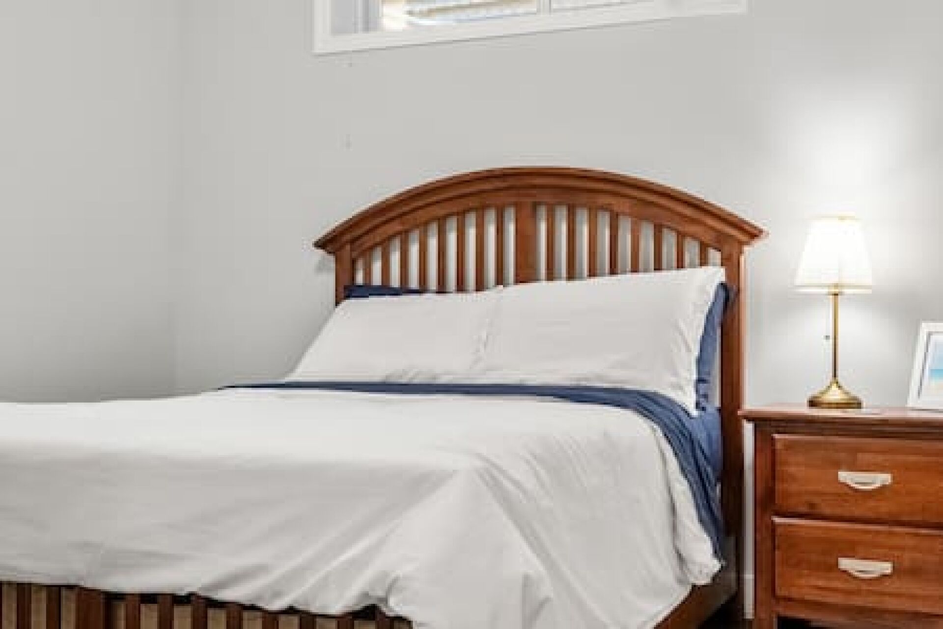 A bed with a wooden headboard, a bedside table with a lamp, and a window above the bed.