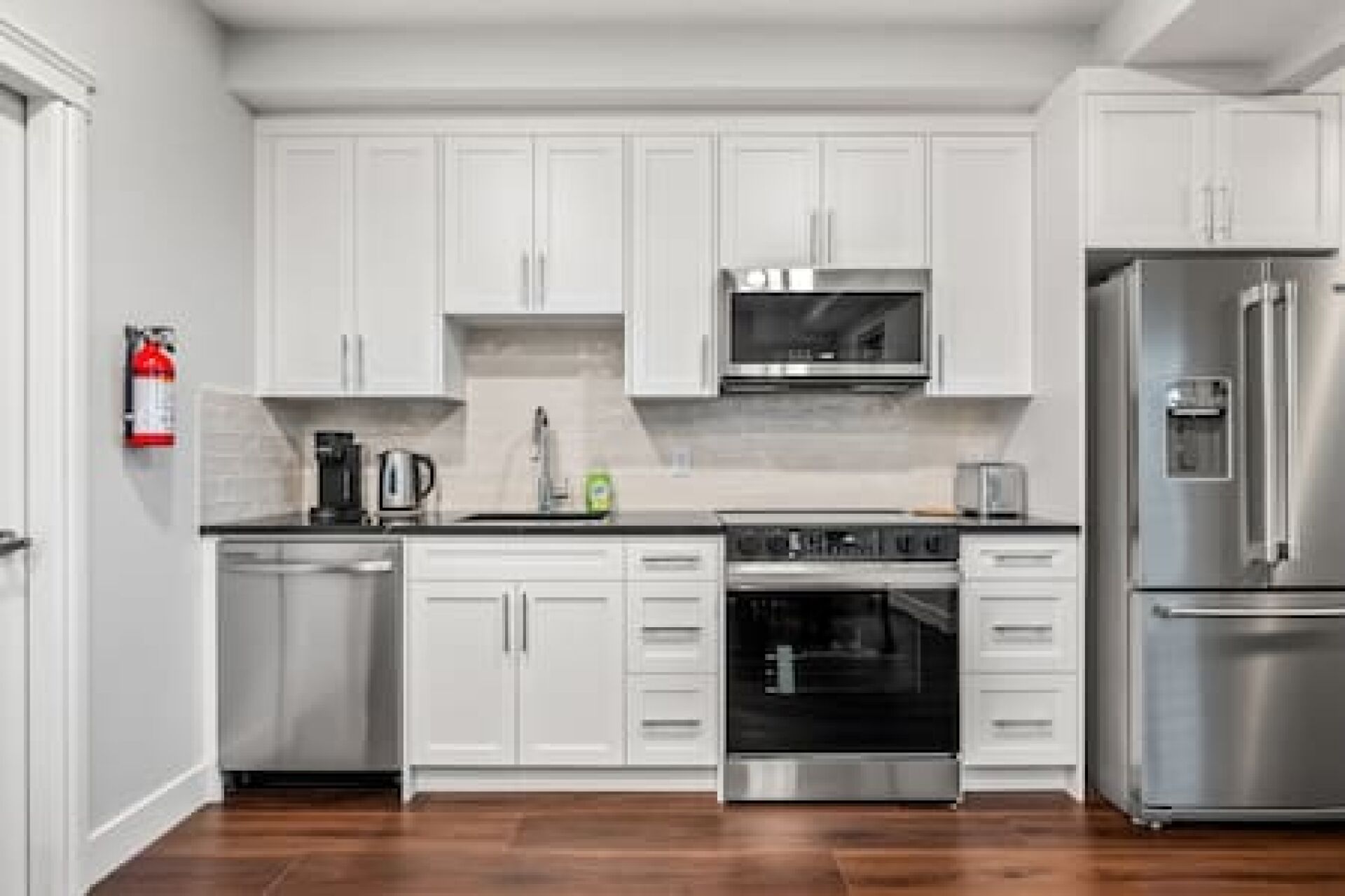 A modern kitchen with white cabinets, stainless steel appliances, and a wooden floor.