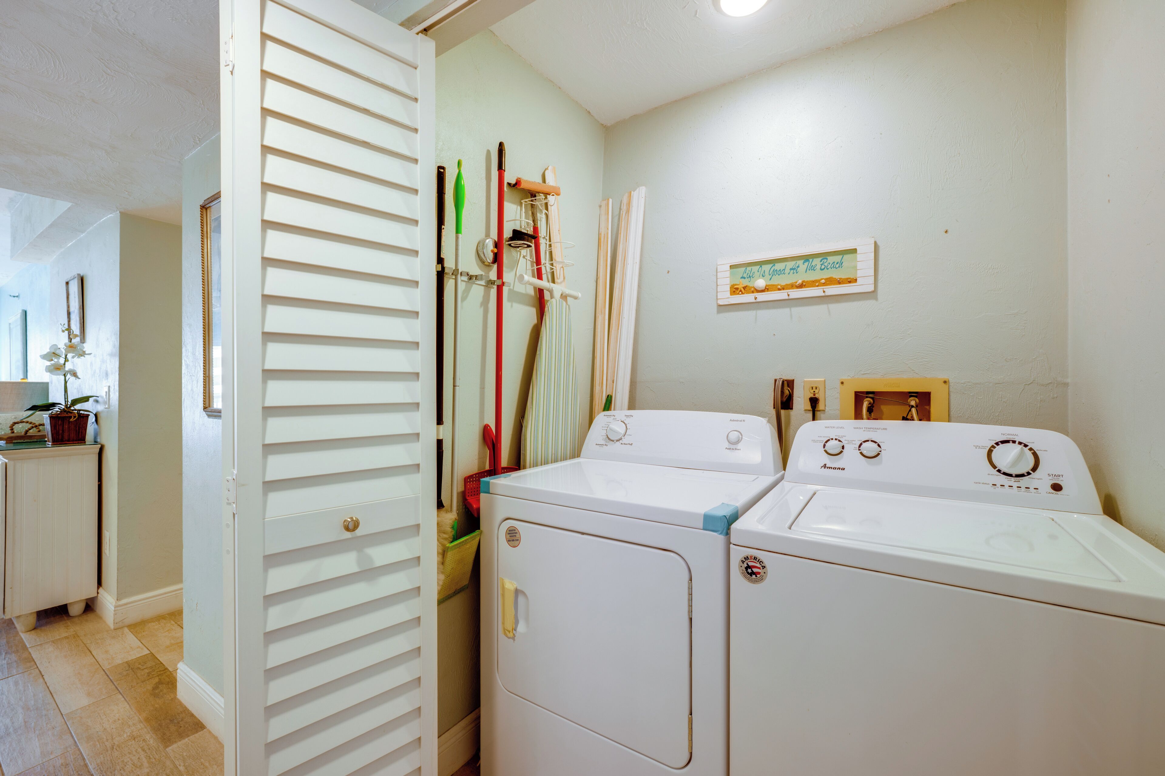 A laundry room with two front-loading washing machines, a drying rack, and a wall-mounted sign.