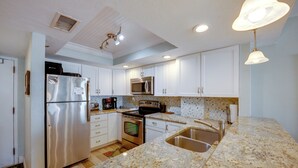 Una cocina moderna con armarios blancos, electrodomésticos de acero inoxidable, encimera de granito y horno integrado.