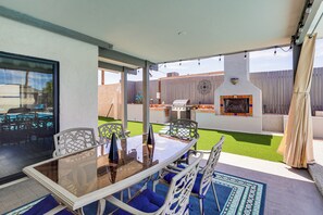 Eine Terrasse im Freien mit einem Glastisch, blauen Sitzmöglichkeiten, einem Grill und einer dekorativen Wand.