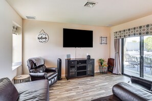 A living room with a flat-screen TV, leather sofas, a black entertainment unit, and a sliding glass door to the outside. - Game Room, Pool & Lake Fun at 'indian Land Oasis' (Lake Havasu City)