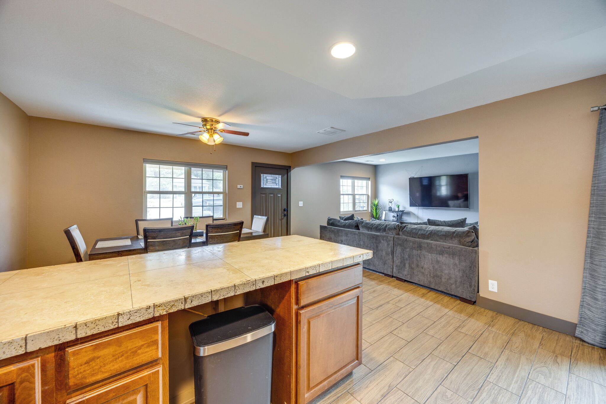 A spacious kitchen with a central island, a dining area, a living room with a sofa, and a TV mounted on the wall.