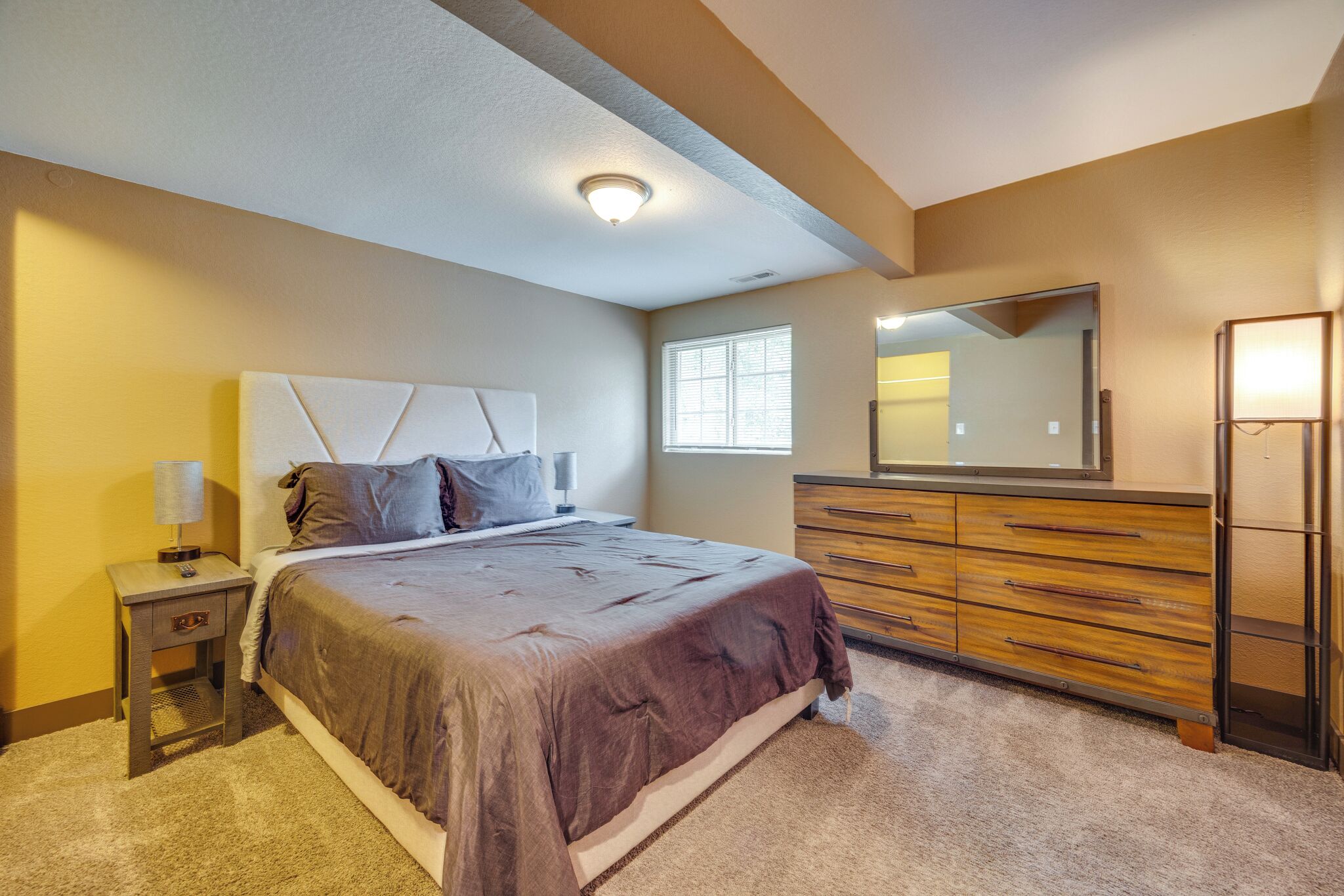Un dormitorio con cama, mesita de noche, cómoda y espejo.