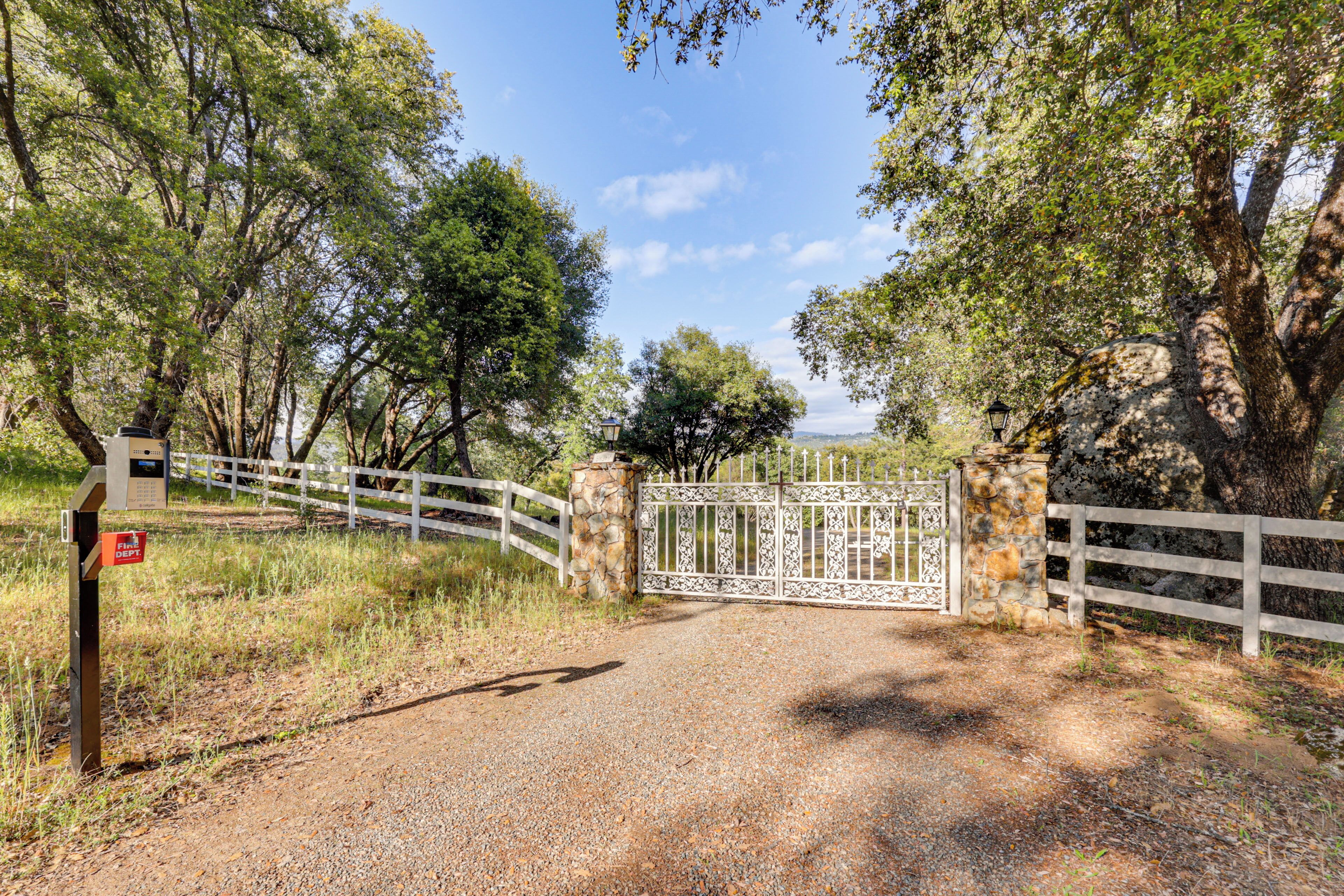 A gravel path leading to a gated entrance with a white fence and a stone wall.