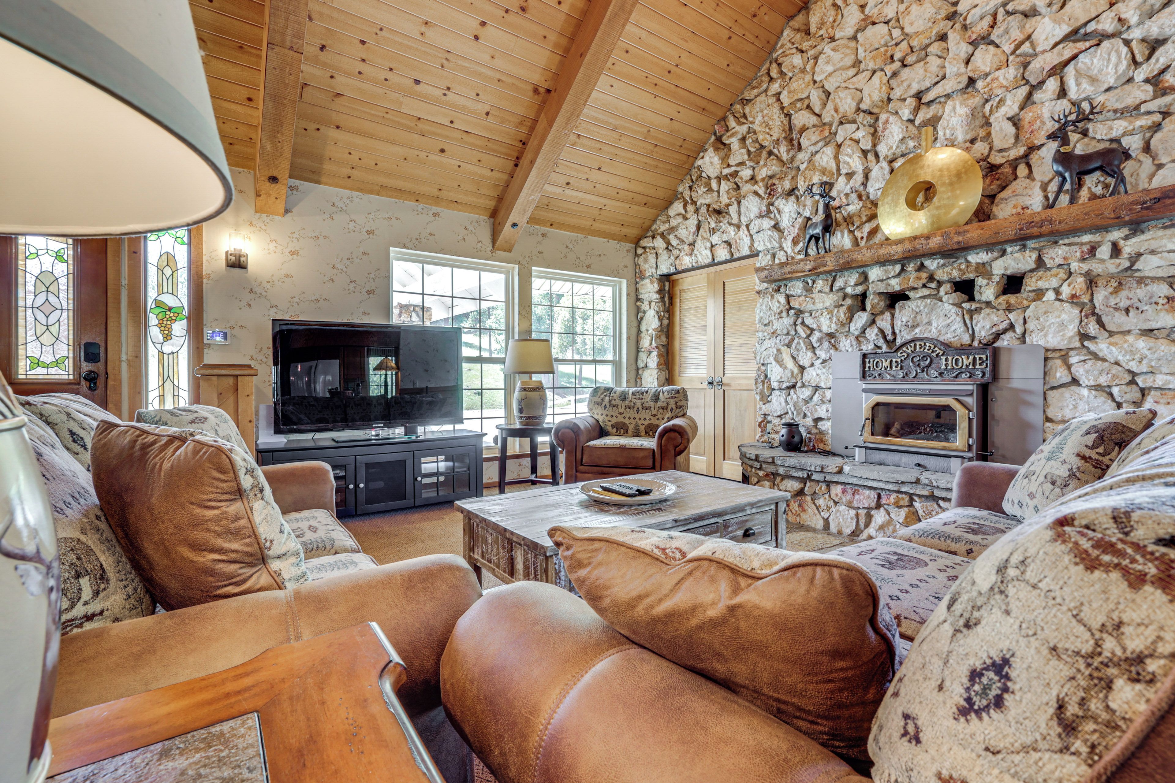 A cozy living room with a stone wall, wooden ceiling, leather sofas, a fireplace, and a television.
