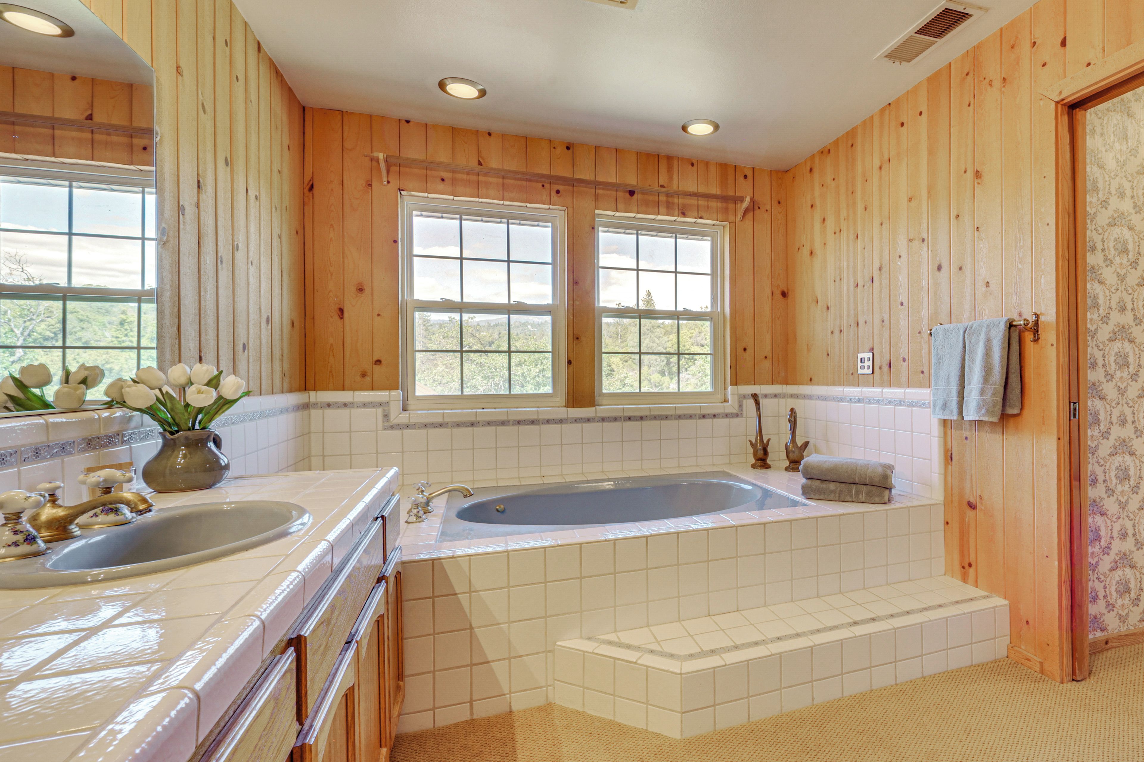 Un baño con paredes de madera, una bañera, un lavabo y una ventana con vistas.
