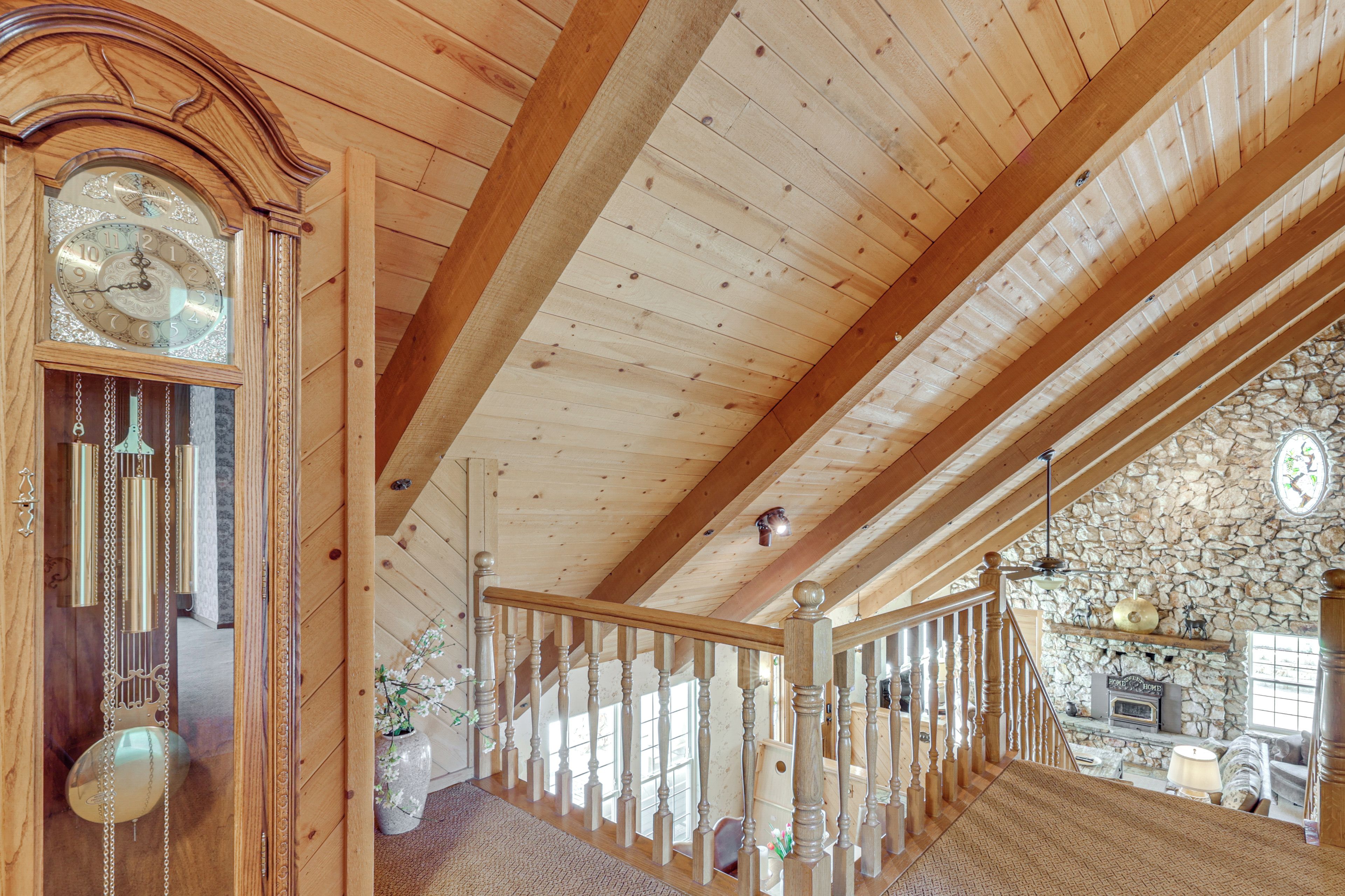 A wooden interior with a large clock, wooden beams, a stone wall, and a staircase.