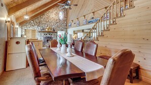 A wooden dining area with a table, chairs, a ceiling fan, and a stone wall. - 25-acre Hideaway in Oakhurst: Pet Friendly! (Oakhurst)