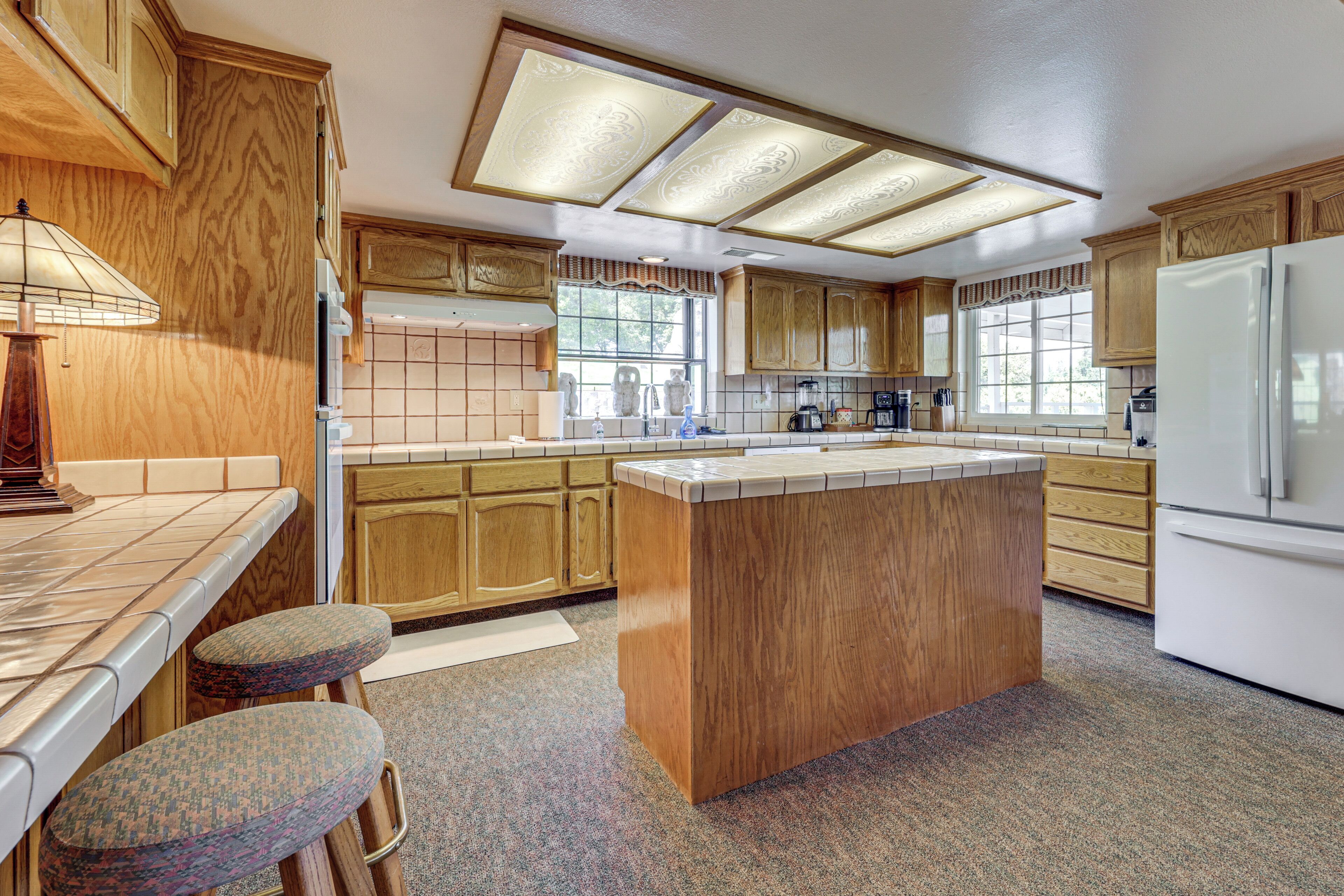 A kitchen with wooden cabinets, a central island, bar stools, and a refrigerator.