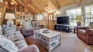 A spacious living room with a wooden ceiling, a fireplace, a television, and a staircase leading to an upper level. - 25-acre Hideaway in Oakhurst: Pet Friendly! (Oakhurst)