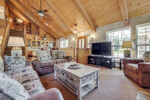 A spacious living room with a wooden ceiling, a fireplace, a television, and a staircase leading to an upper level. - 25-acre Hideaway in Oakhurst: Pet Friendly! (Oakhurst)