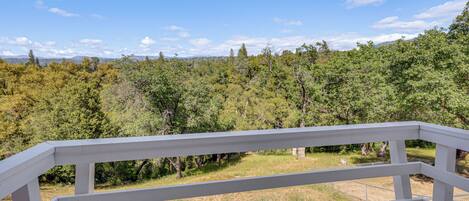 A white balcony railing overlooking a forested area with a clear sky.