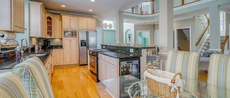 A spacious kitchen with wooden cabinets, a dining area with striped upholstered chairs, and a glass-top table.