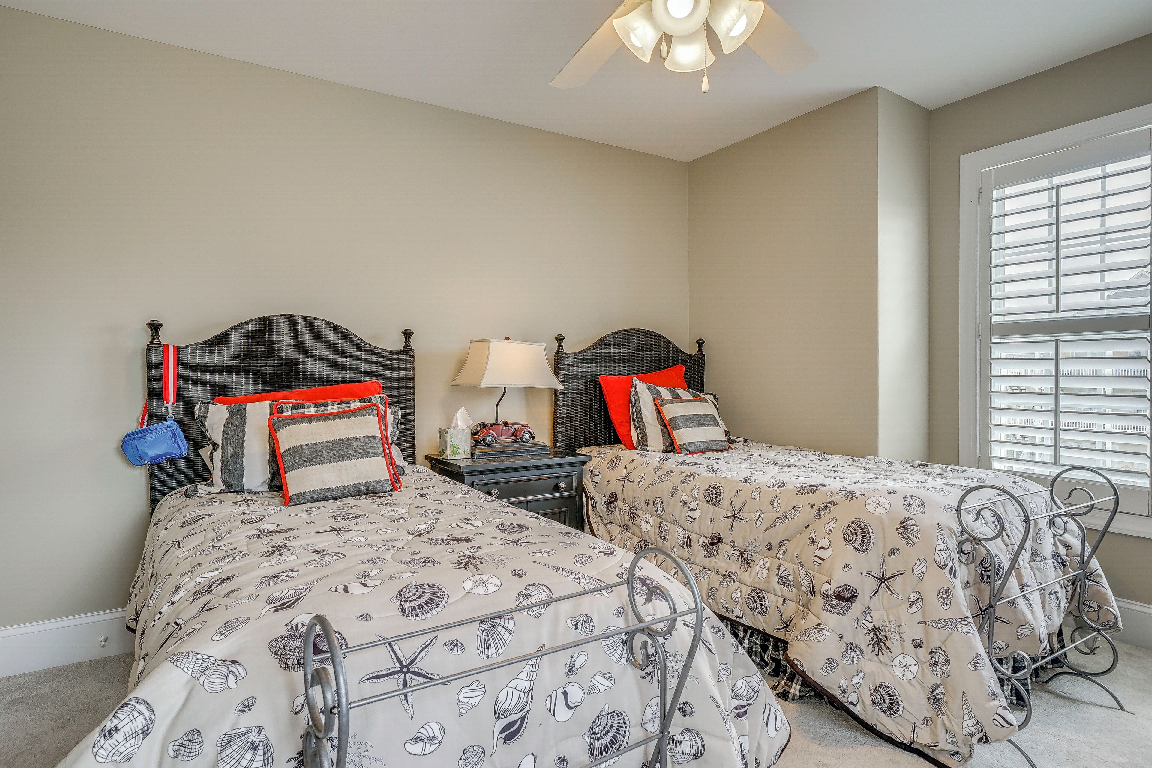 A bedroom with two beds, a nightstand, a lamp, and a window with blinds.