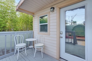 A covered porch with two white metal chairs and a small table, a sliding glass door, and a window with a view of a green shed. - Tiny House Experience in Las Vegas w/ Free Parking (Las Vegas)